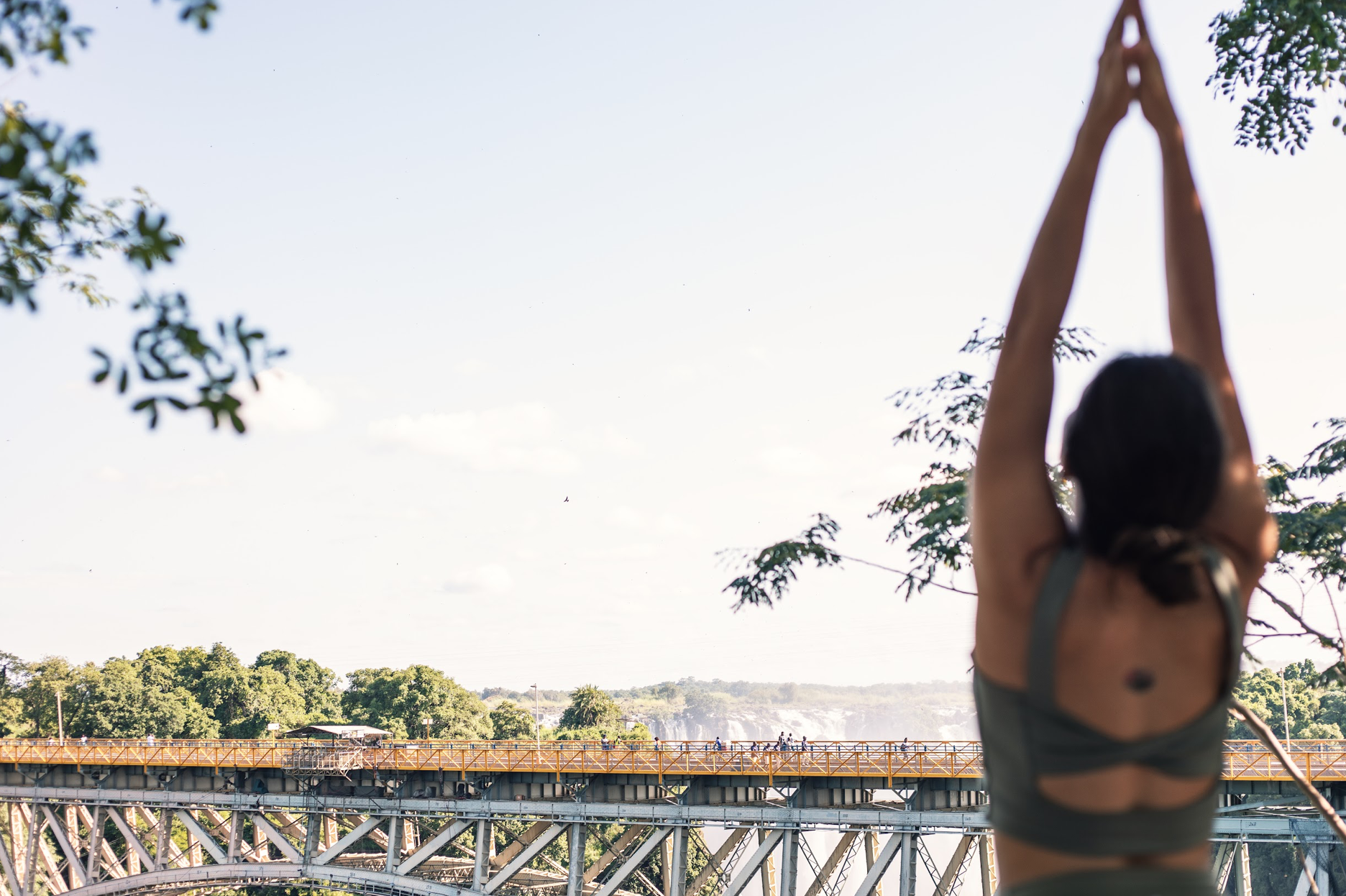 Guest with arms raised in yoga pose facing the Victoria Falls Bridge