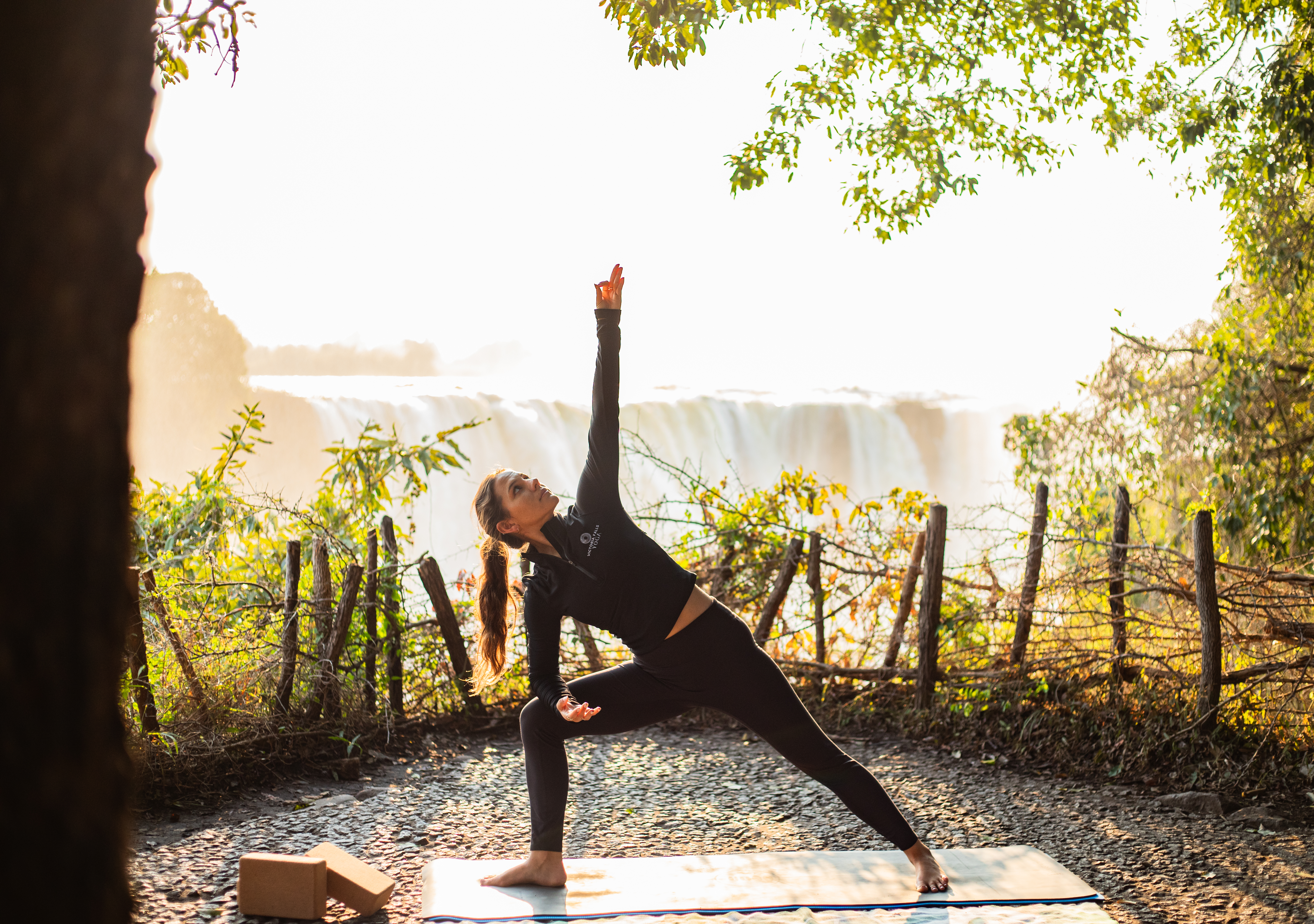 Guest in extended side angle pose beneath a tree overlooking Victoria Falls