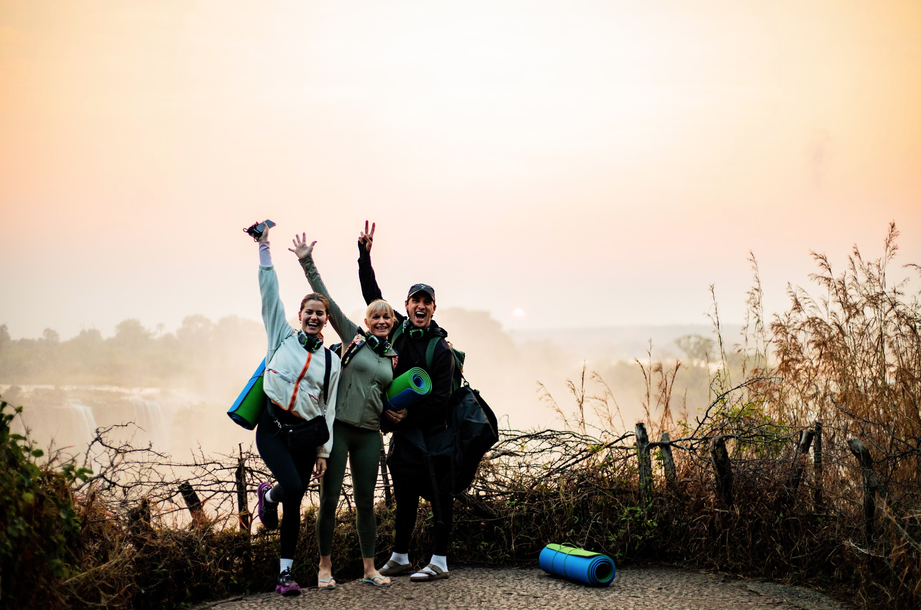 Group celebrating with yoga mats above Victoria Falls at sunrise