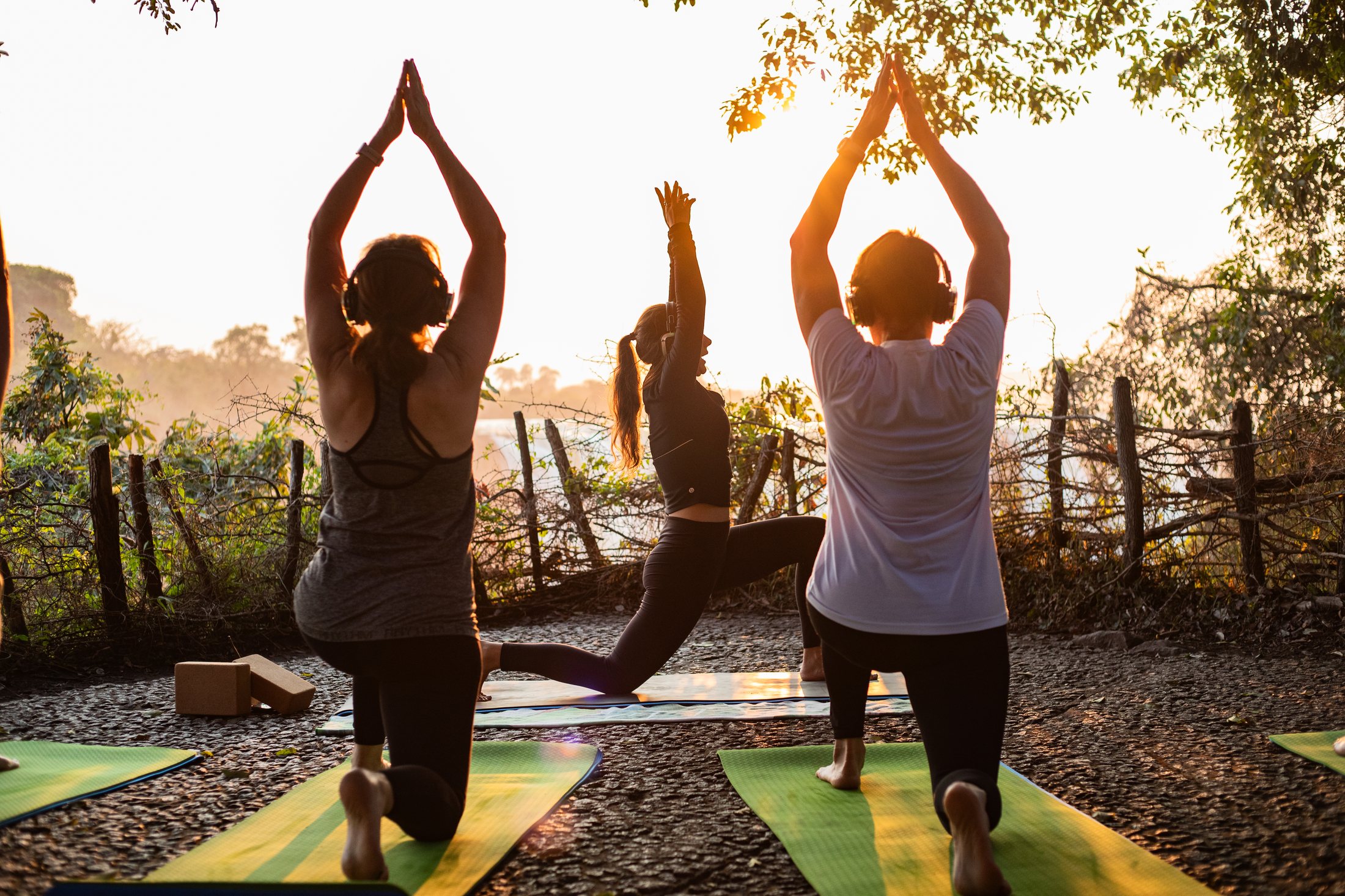 Three yogis in warrior pose at sunrise above Victoria Falls