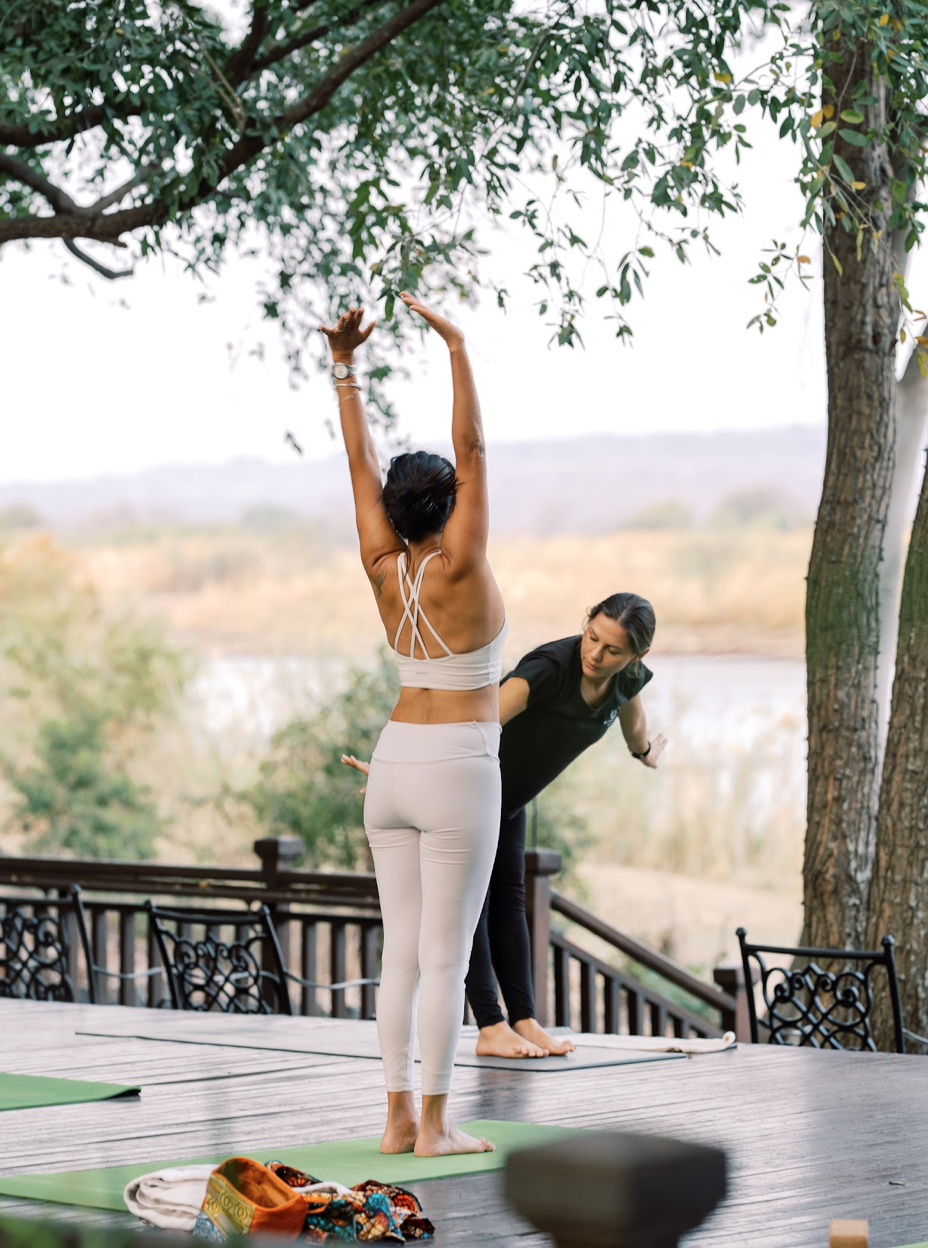 Instructor adjusting a guest's pose on a deck overlooking the river